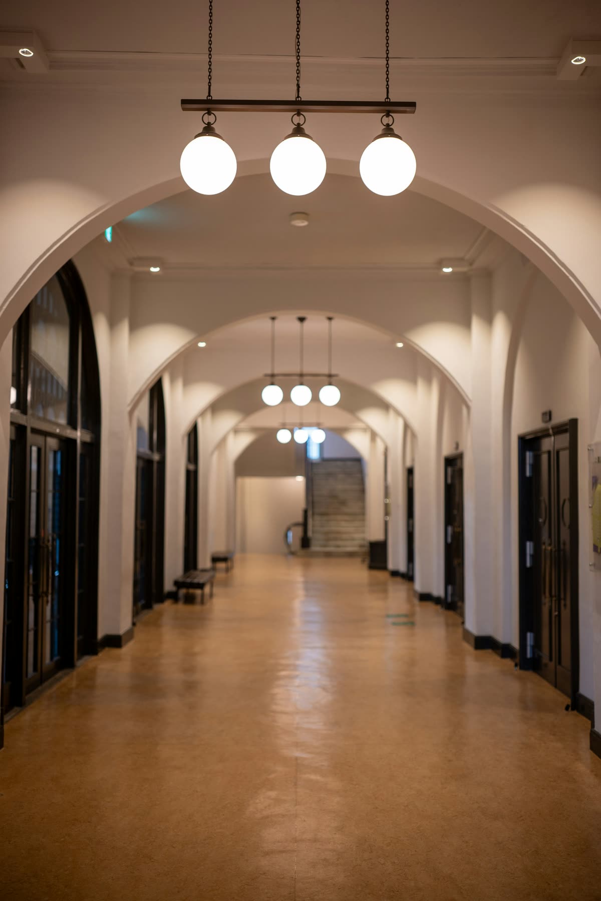 A long hallway with a run of white plastered arches across the ceiling and pendant lights hanging between them.